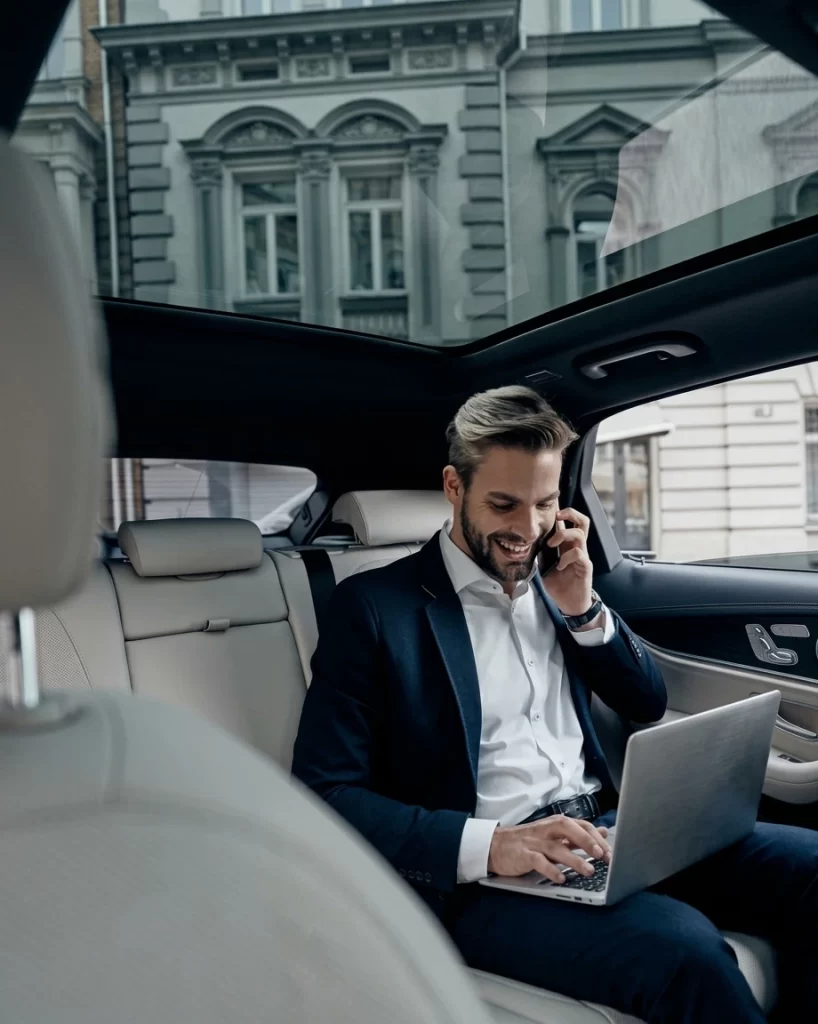 Uśmiechnięty klient korzystający z laptopa i telefonu podczas podróży komfortową taksówką Radio Taxi Cieszyn